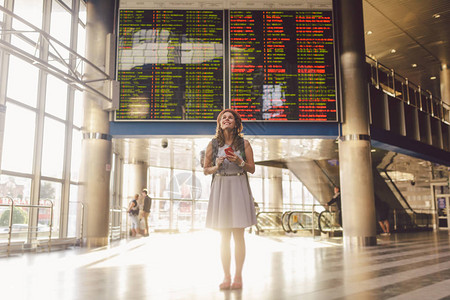 美丽的年轻白种女人穿着裙子和背包站在火车站或航站楼内背景图片