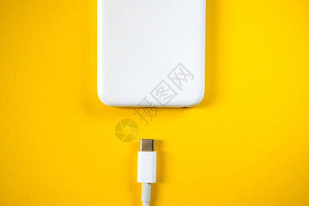 智能手机通过黄色背景上的电缆连接到充电器复制空间图片