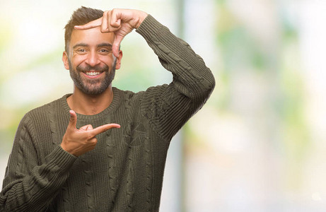 身穿冬毛衣的成年西班牙男子在孤立的背景中微笑地用手和指搭架图片