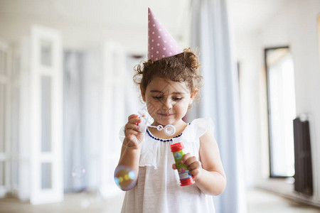 可爱笑的小女孩穿着深色卷发穿着裙子和生日帽子在家中图片