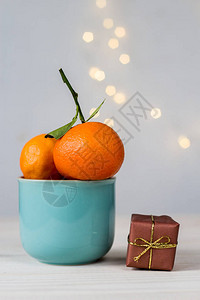 蓝色陶瓷杯和小礼物盒中的有机橘子白底图片