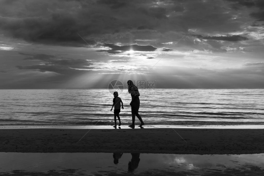 母亲和儿子在日落的沙滩上以黑图片