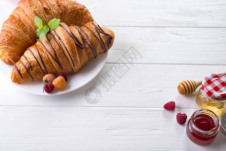 经典的法式羊角面包与白色木制背景上的浆果图片