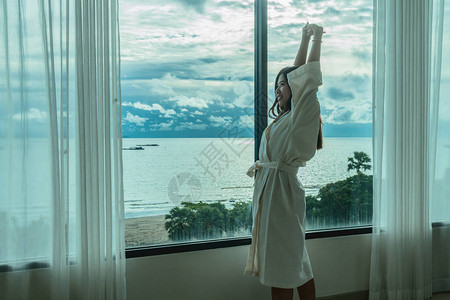 穿浴衣的亚裔妇女早上在豪华酒店从床上醒来时图片
