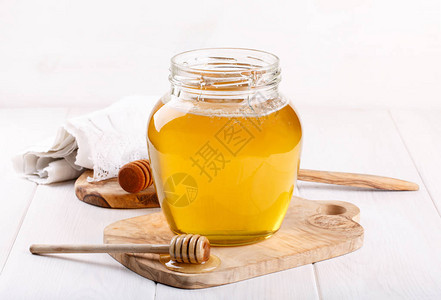 玻璃瓶的蜂蜜和白色的木制花图片