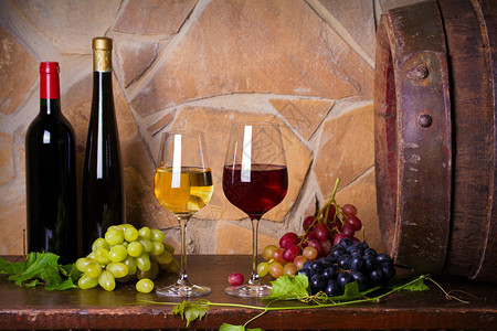 酒窖里的旧木桶旁边有葡萄的红白葡萄酒杯和酒瓶背景图片