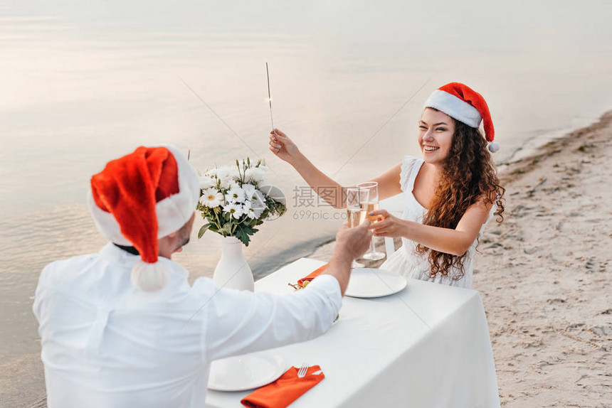 穿着圣塔帽的年轻夫妇庆祝圣诞节与香槟杯连在图片