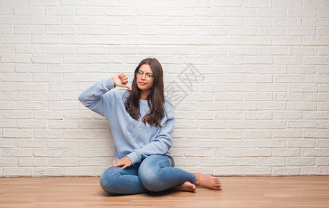 白砖墙上坐在地上的青褐色年轻女人图片