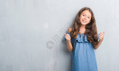 年轻的西班牙裔孩子在灰墙成功的标志上用手做积极的手势图片