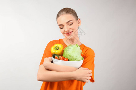 年轻女在灰色背景上拿着碗和蔬菜吃图片