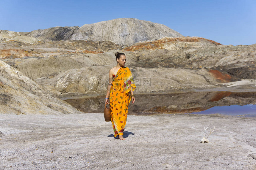 身穿沙里加壶子的年轻女子从一个干旱无生命地区的池塘里冒出来仔细地看图片