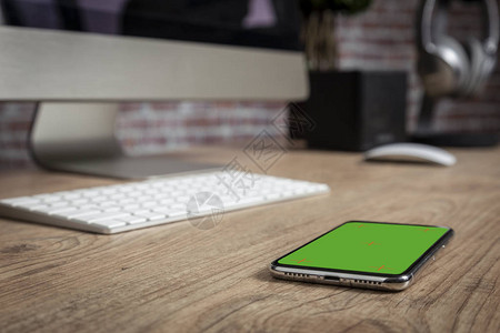 在办公室前面的木制桌子顶部有全屏智能手机绿色屏幕录图片