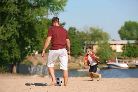 小男孩和他爸在沙滩上踢足球图片
