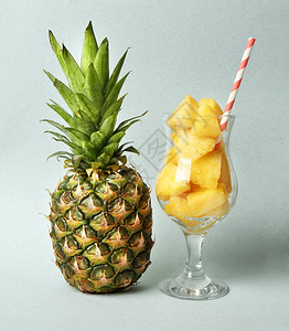 浅色背景下装有菠萝罐头和整个水果的玻璃杯图片