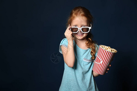 可爱的小女孩与一杯爆米花穿着3D电影眼镜图片
