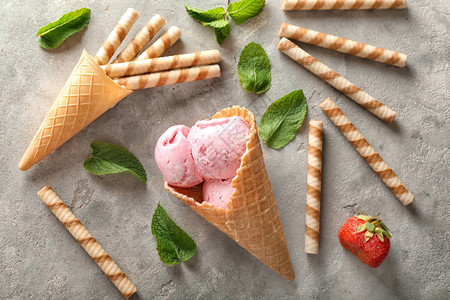 华夫蛋筒配美味的草莓冰淇淋和灰色背景的棍子图片