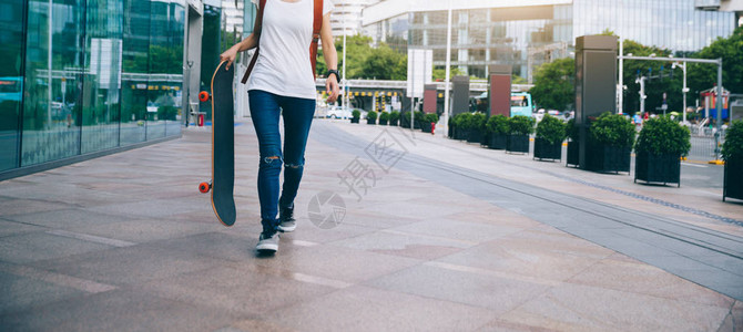 妇女滑板车手拿着滑板在城图片