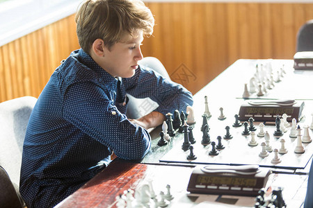 穿着蓝衬衫的聪明可爱男孩在课堂棋盘上下棋爱好课图片