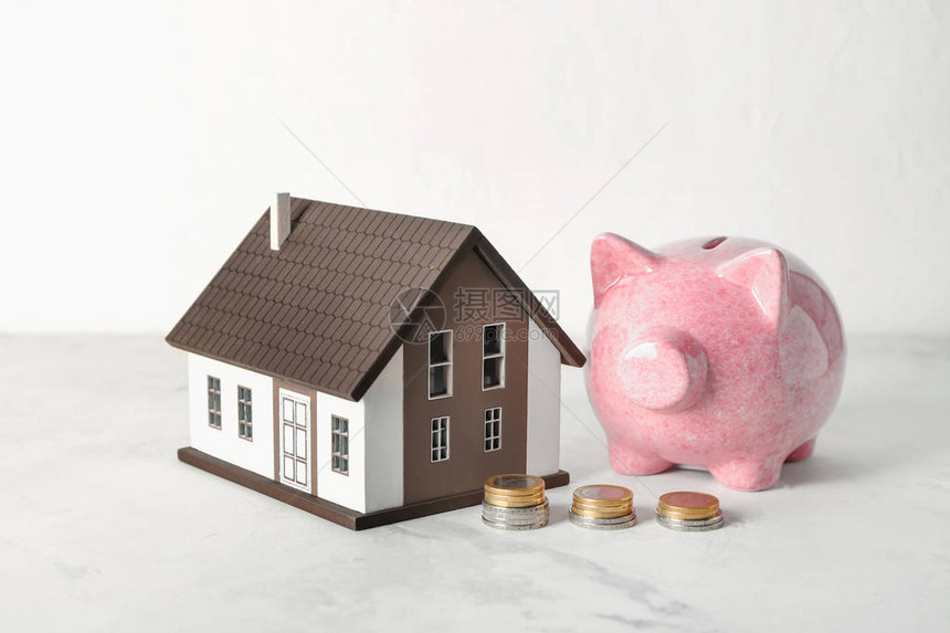 房子模型存钱罐和白桌上的硬币抵押贷款概念图片