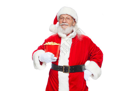 戴着白手套的微笑善良的圣诞老人一只手拿着一个装有爆米花的红色桶图片