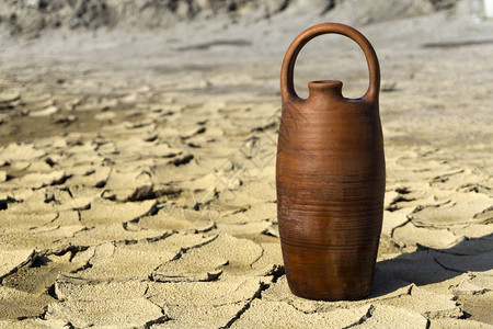 陶瓷壶与水站在干裂的粘土沙漠土地中间背景图片