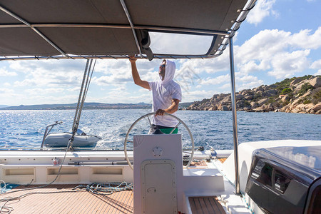 迷人的男船长在阳光明媚的夏日在平静的蓝色海水中驾驶这艘花式双体船帆图片