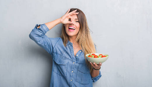 青成年女子在灰墙边吃着健康的番茄沙拉面笑得开心手对眼睛用手看着手图片