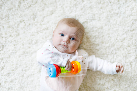 可爱的新生婴儿在白色背景上玩五颜六色的拨浪鼓玩具图片