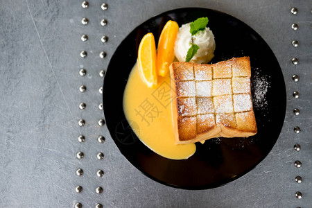 蜂蜜吐司在黑色盘子中装饰了生奶油和橙子水果片图片