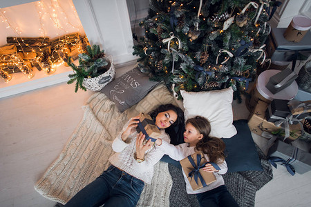 母亲和女儿带着礼物躺在圣诞树图片