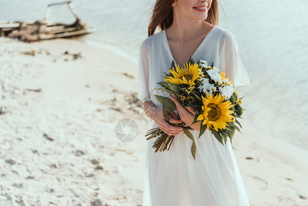 在海滩上拿着带向日葵花的束的笑图片