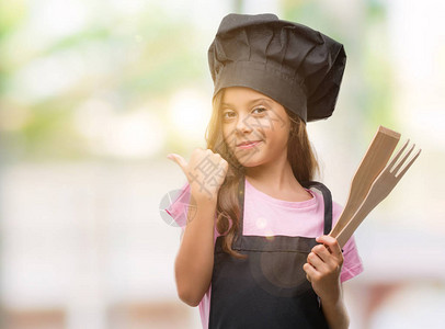 身穿厨师制服的褐发西班牙裔女孩指着拇指朝一图片