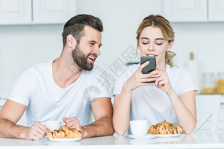 年轻男子在早餐时用智能手机看着女朋友图片