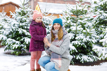 快乐的孩子女儿和穿着冬装的年轻女人在圣诞市场上选择圣诞树图片