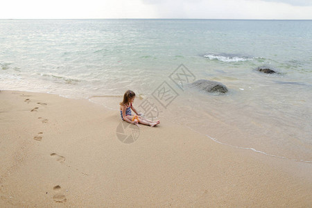 小女孩坐在海边沙滩上玩洋娃图片