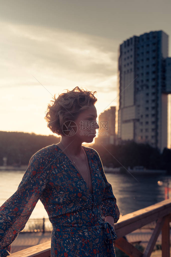 女人站在离河岸附近的木制楼梯上在日落时分的一个城市风景公园图片