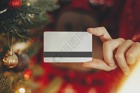 手拿着信用卡特写的美丽圣诞树与节日房间里的灯光圣诞购物和销售理念折扣图片