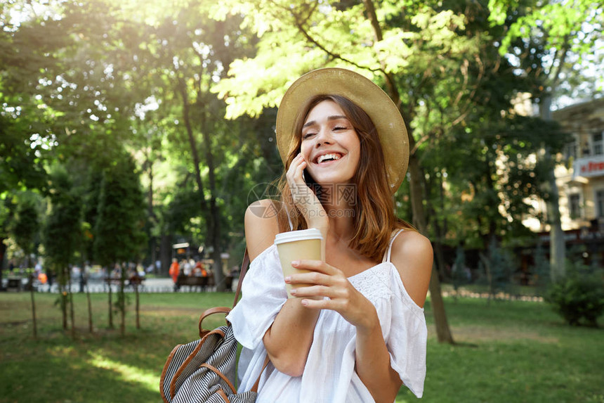 微笑迷人的年轻女子的户外肖像戴着时尚的帽子背包和白色夏装图片