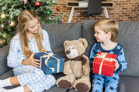 穿着睡衣快乐的孩子带着圣诞礼物和看泰迪熊图片