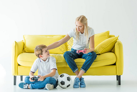 母亲在白色的黄色沙发上玩电子游戏时抚摸儿子图片