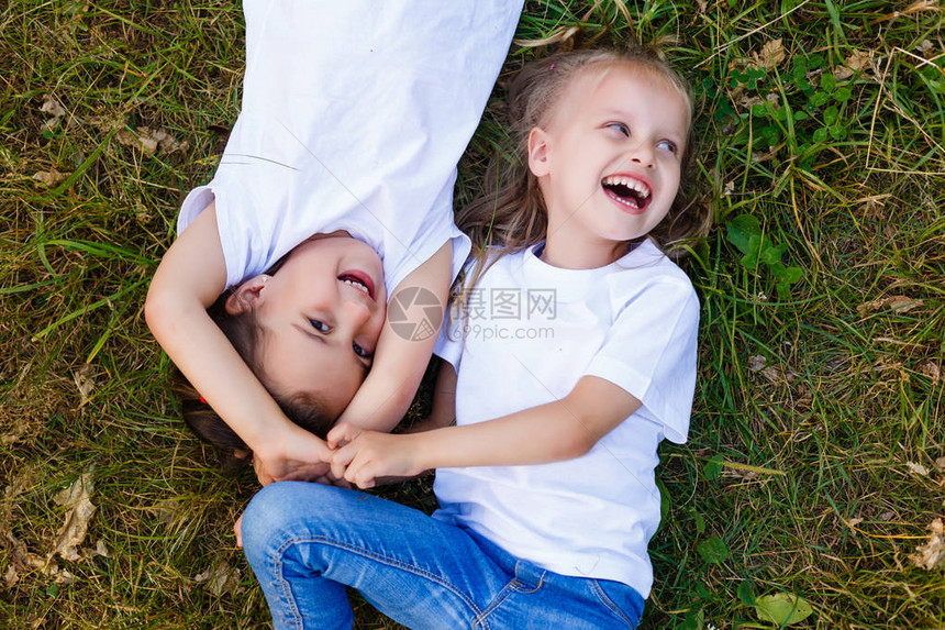 两个穿白色T恤衫的小女孩躺在公园的草地图片