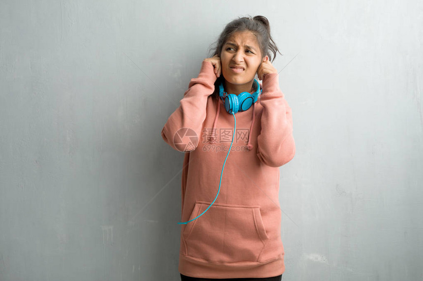 年轻运动的印度女人站在墙上用双手遮住耳朵图片