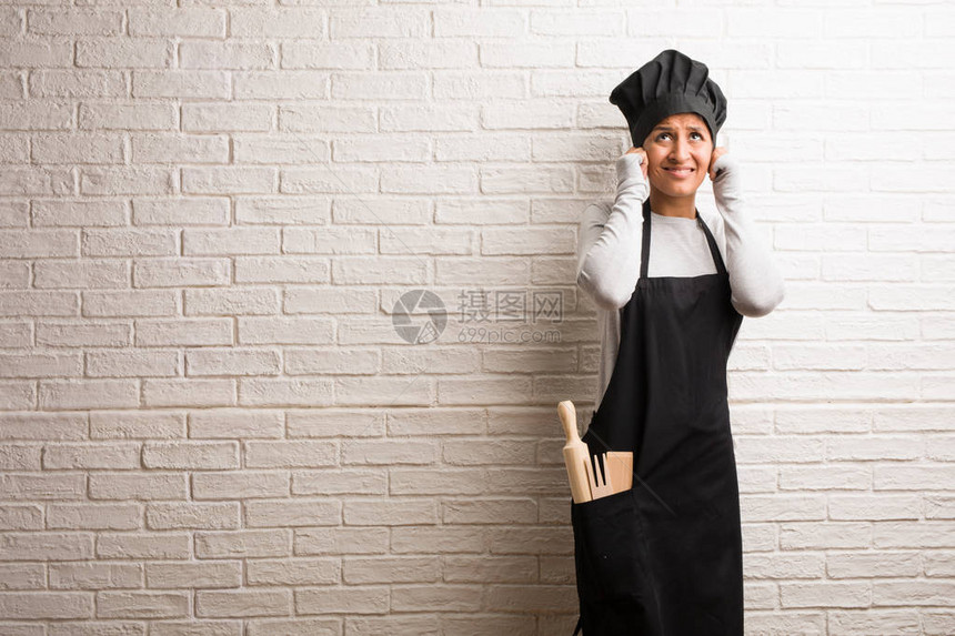 年轻的面包师印度年轻女人对着一堵砖墙用双手遮住耳朵愤怒和厌倦图片