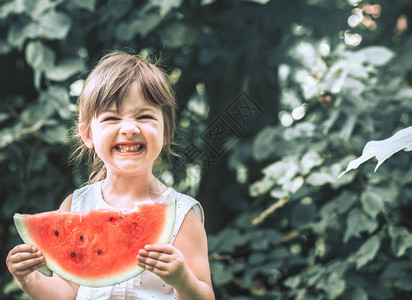 自然背景下带一块西瓜的微笑小女孩婴儿食品的概念和图片