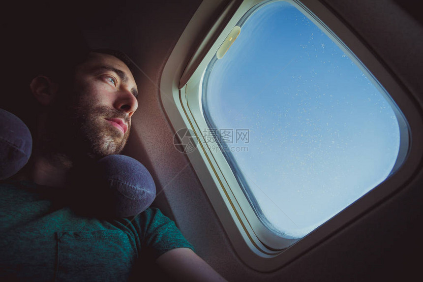 带着颈枕的沉思男人透过飞机的窗户向外看图片