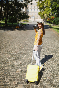 穿着黄色衣服的快乐旅行者旅游女人带着手提箱在复古老式照片相机上拍照图片