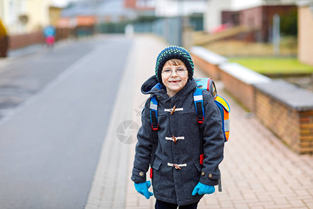 带着眼镜从学校走出来的小男孩街头的孩子学龄前儿童穿着温暖的春秋或冬衣服眼镜和背包快乐的学生或图片