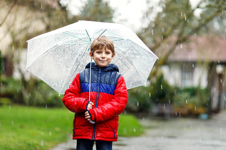 漂亮的小男孩在上学的路上在雨夹雪雨雪中行走图片