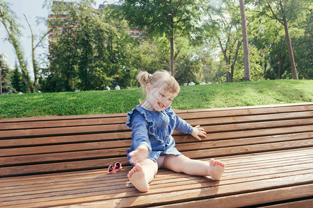 小女孩坐在长椅上在阳光温暖的一天在图片