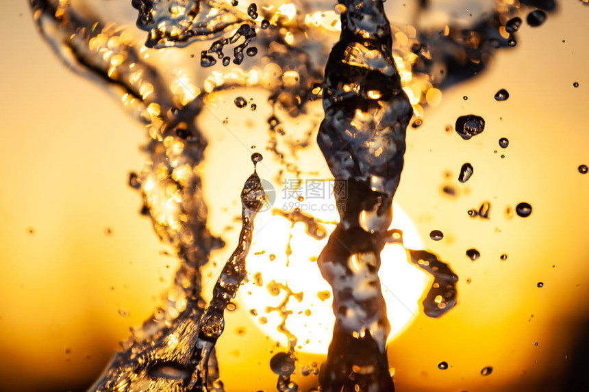 黄橙色背景下阳光下有水滴和气泡的水流的特写镜头一个大喷图片